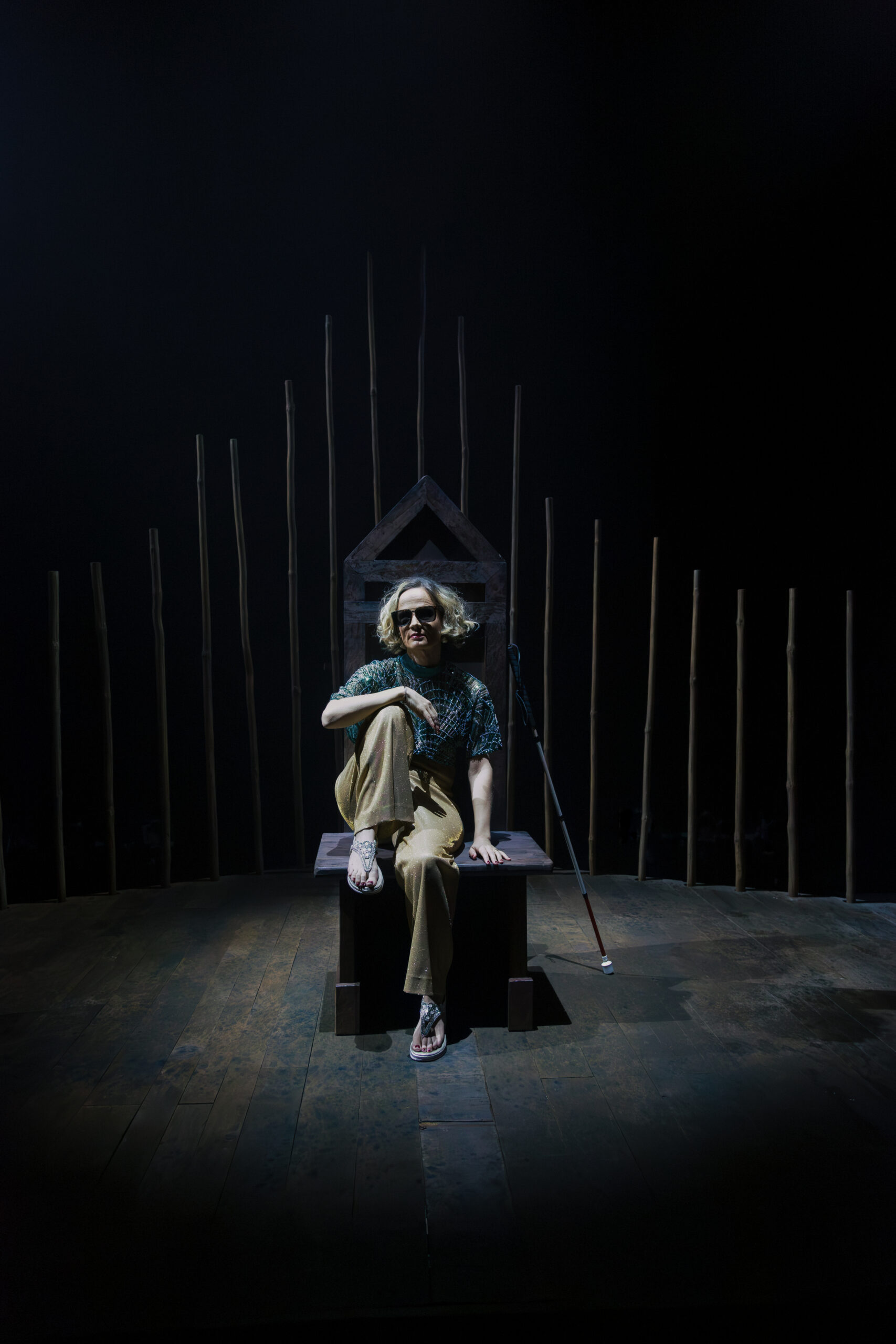 Hanlie Stehl sits in a dark, theatrical setting with her white cane beside her.