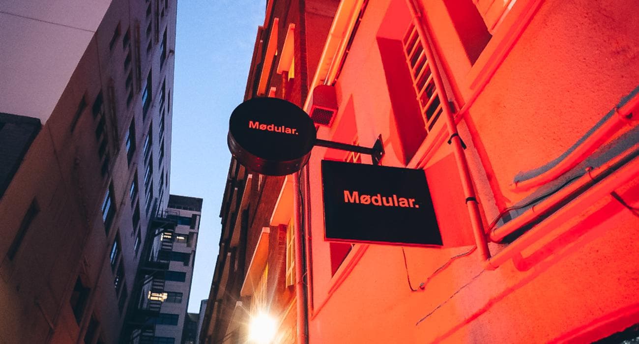 Mødular's round and box signs glow against a red-lit facade on Riebeek Street at dusk.